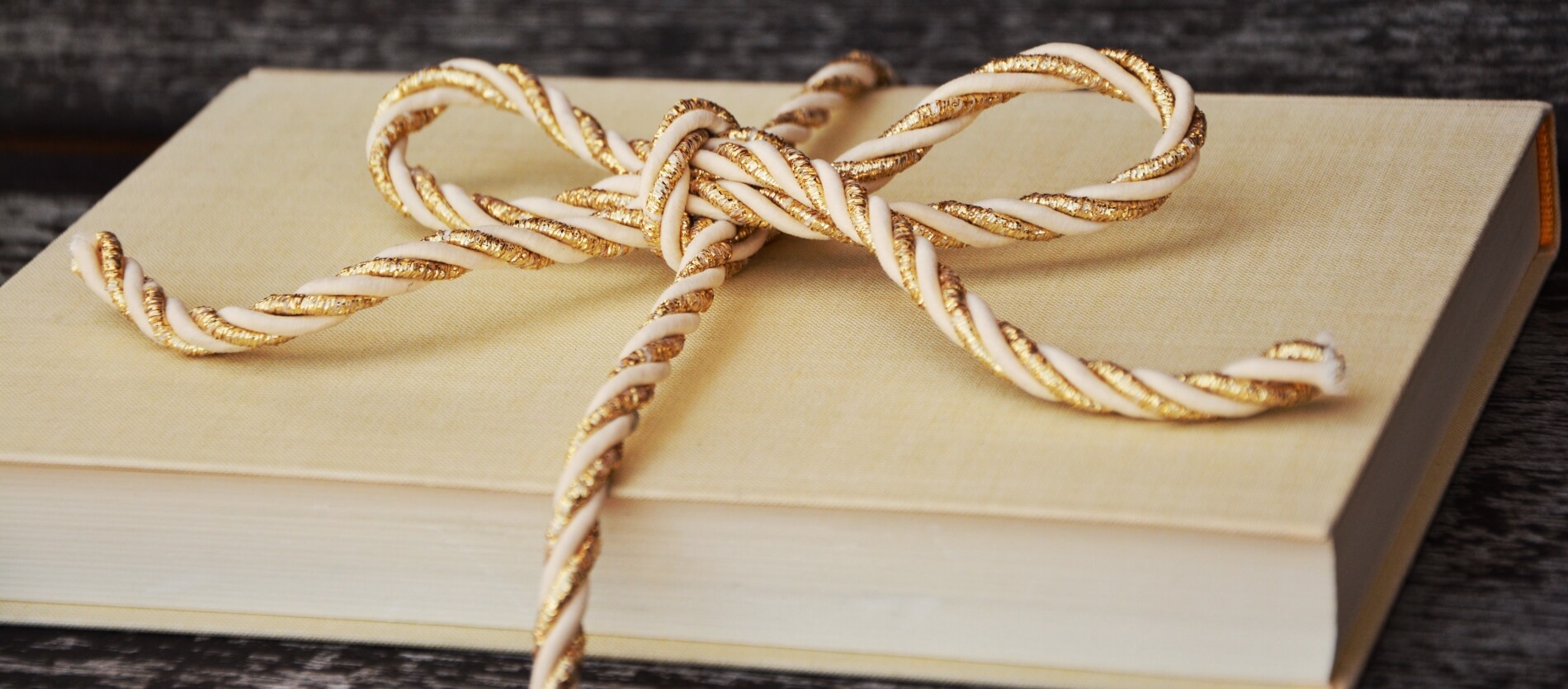 Cream coloured book gift-wrapped in gold and cream coloured rope