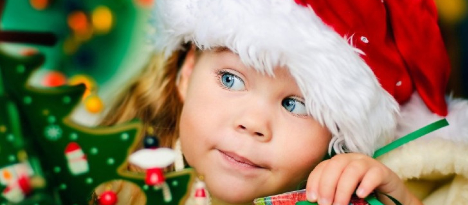A young girl wearing a Christmas hat looking at Christmas decorations