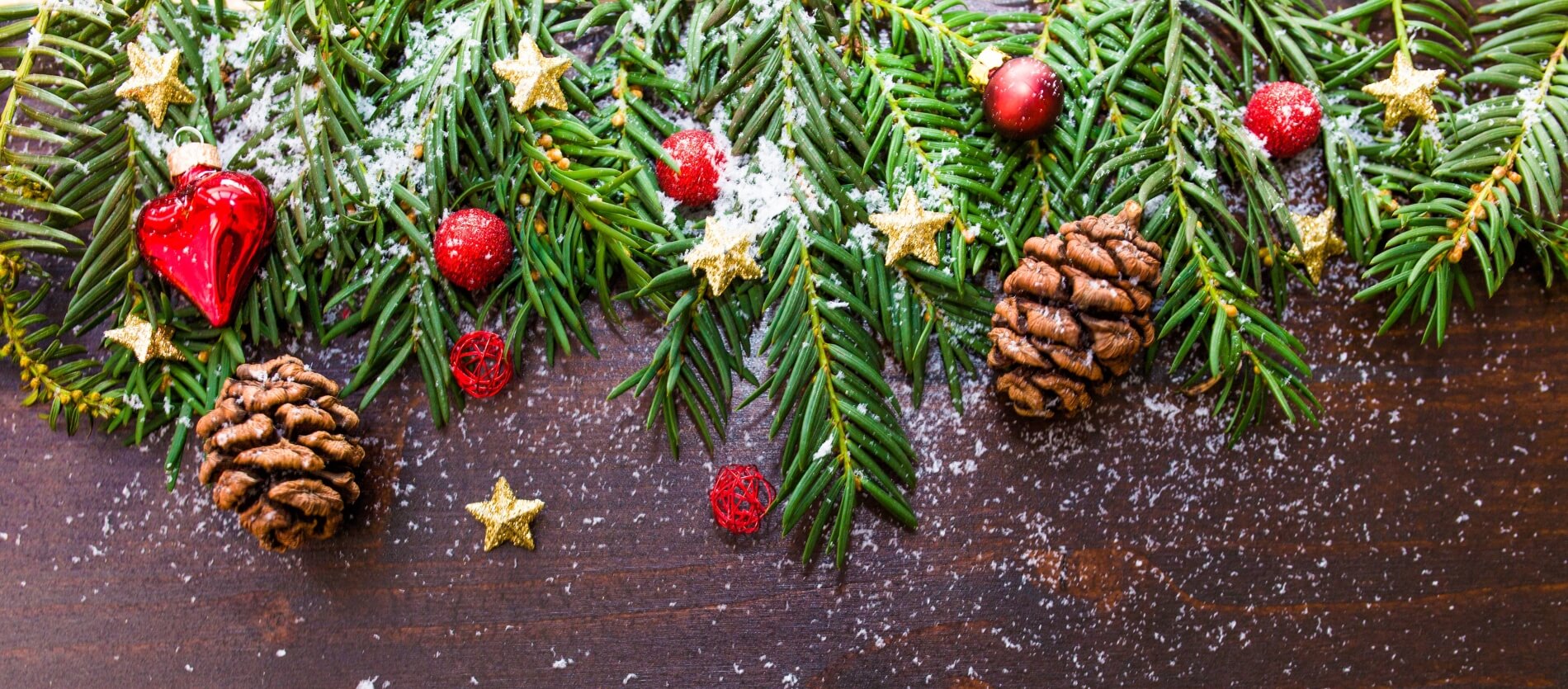 Christmas ornaments with pine cones, red baubles and green pine leaves on a brown wooden surface