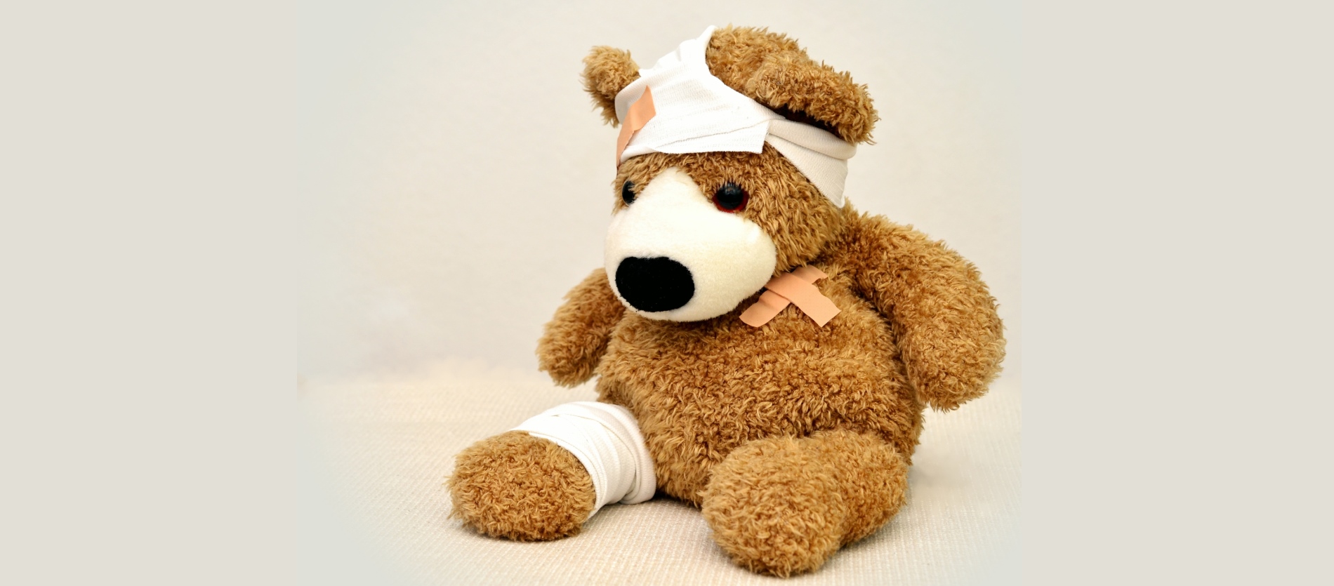 Injured teddy bear with bandaged leg, head and a band-aide on its torso.