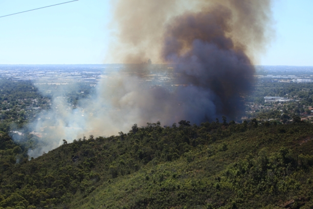 View of a black bushfire smoke rising from a fire on a hill