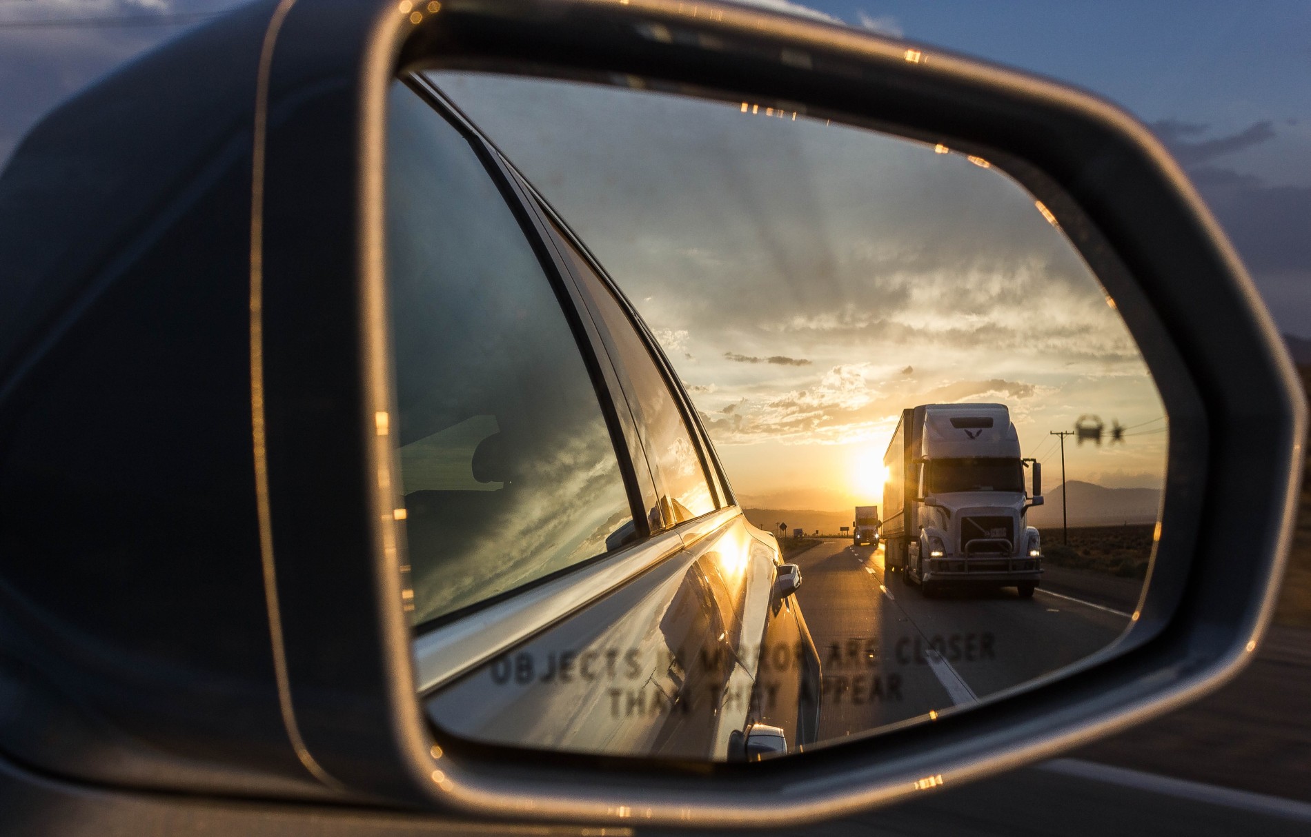 Vehicle side mirror reflecting a heavy haulage truck with the sun setting in the background