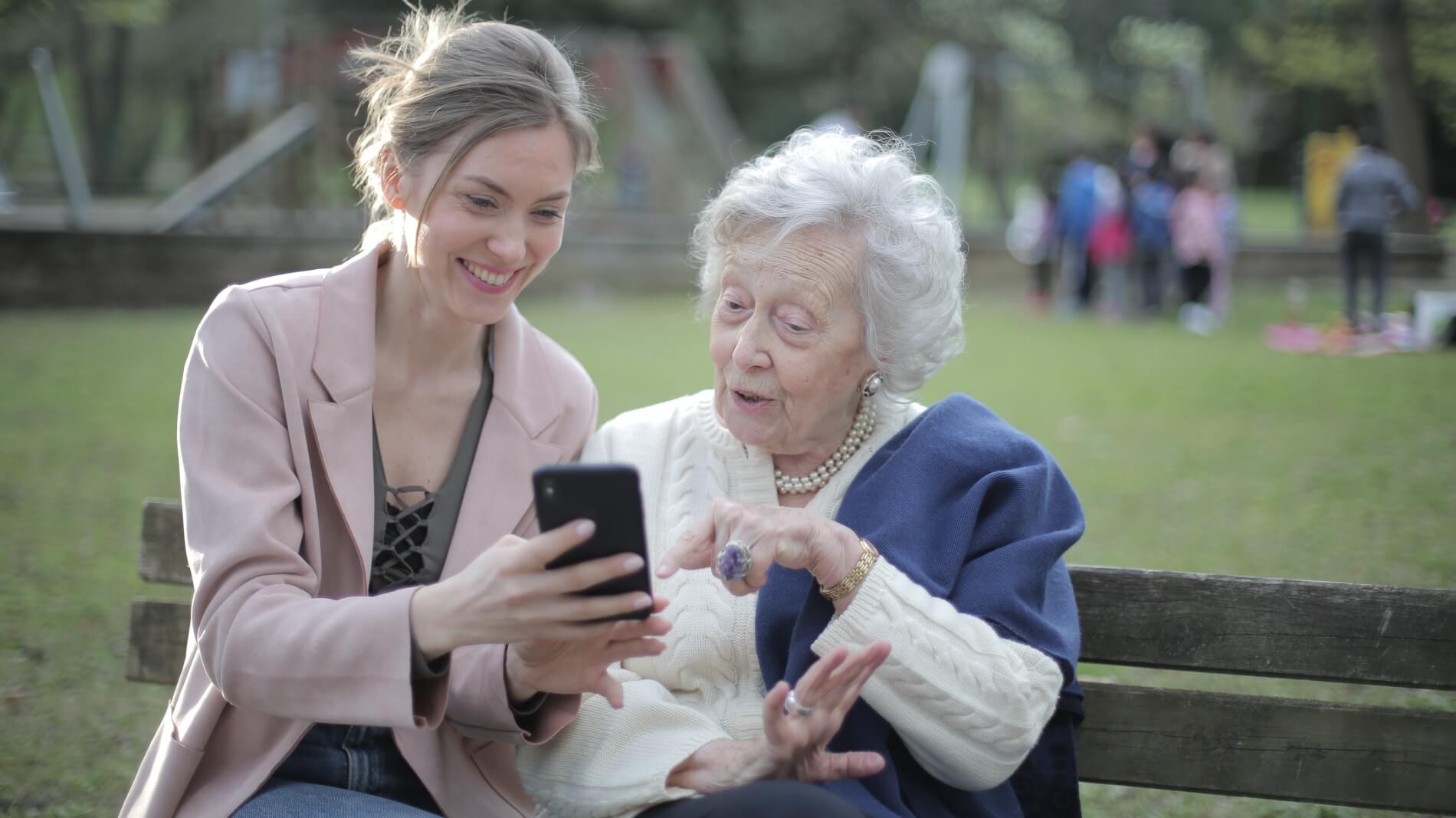 An elderly woman being shown something on a mobile phone by a younger woman