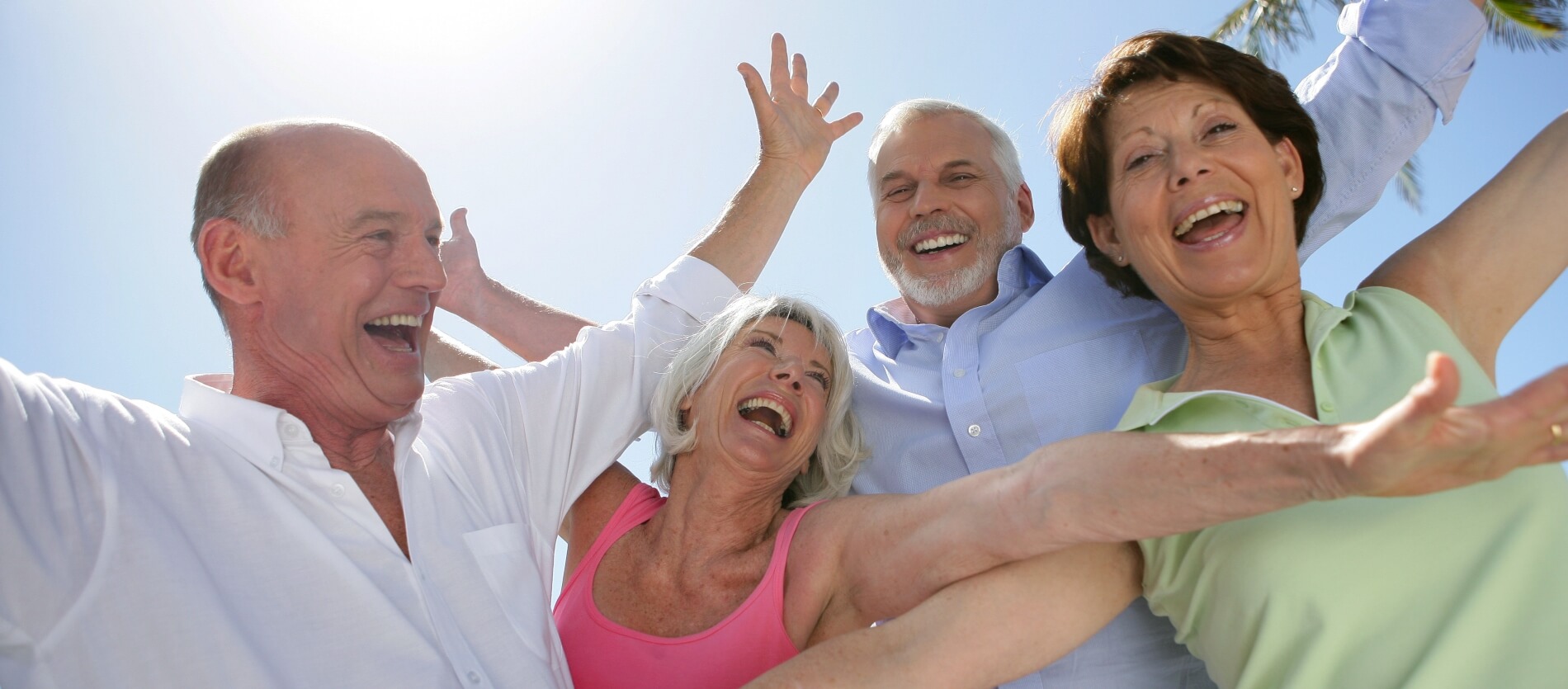 4 senior people with their arms out with blue sky behind them