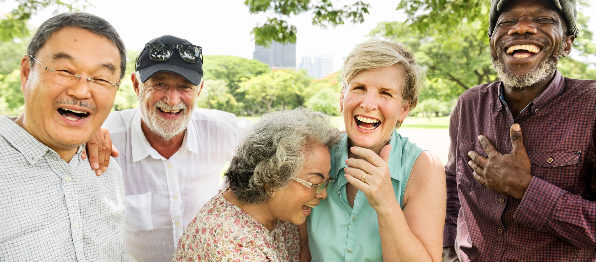 Five older adults laughing in an outdoor park area.