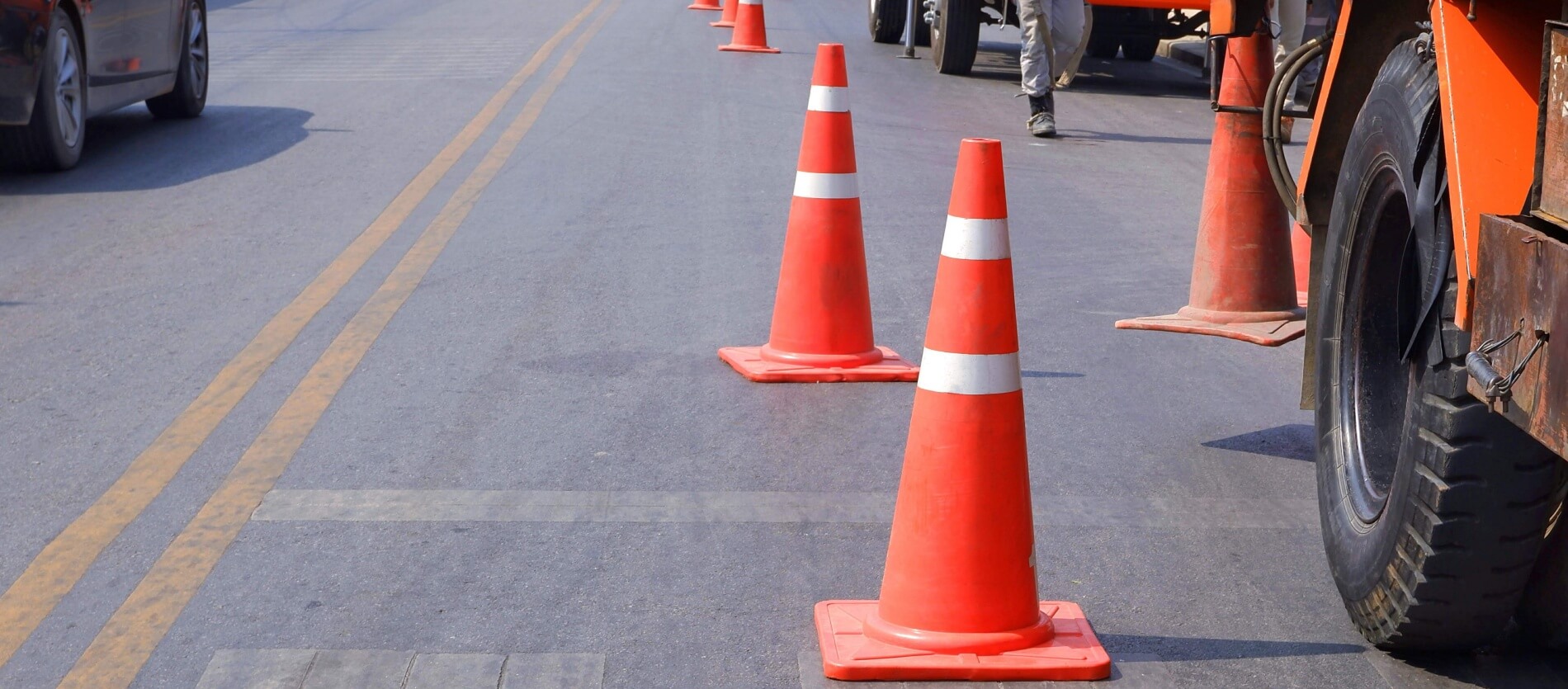 Orange road work cones adjacent to construction trucks on the road