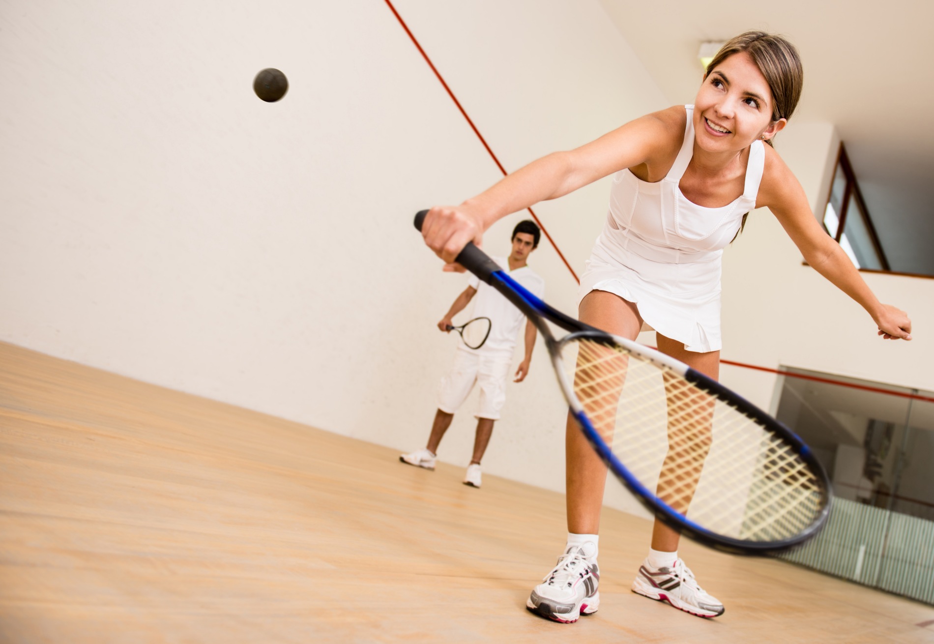 Young lady doing a back hand to return ball in a game of squash