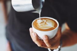 A barista pouring milk into a coffee cup making a heart shape with the milk froth.
